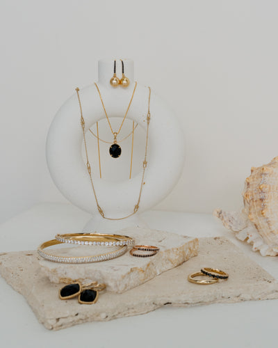 black onyx pendant with other gold necklace hanging. Matching accessories including bangles, earings and black diamond rings laid out infront. 