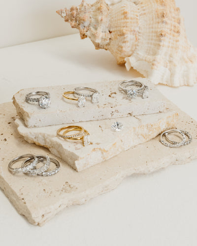 various stackers, wedder and engagement rings placed around a stone bench